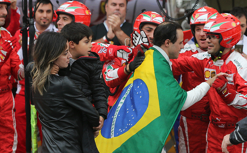 Williams' Felipe Massa of Brazil wears his country's flag over his shoulders and is followed by his wife and son as he is greeted by members of the Ferrari team after he had to withdraw from the race due to car problems.